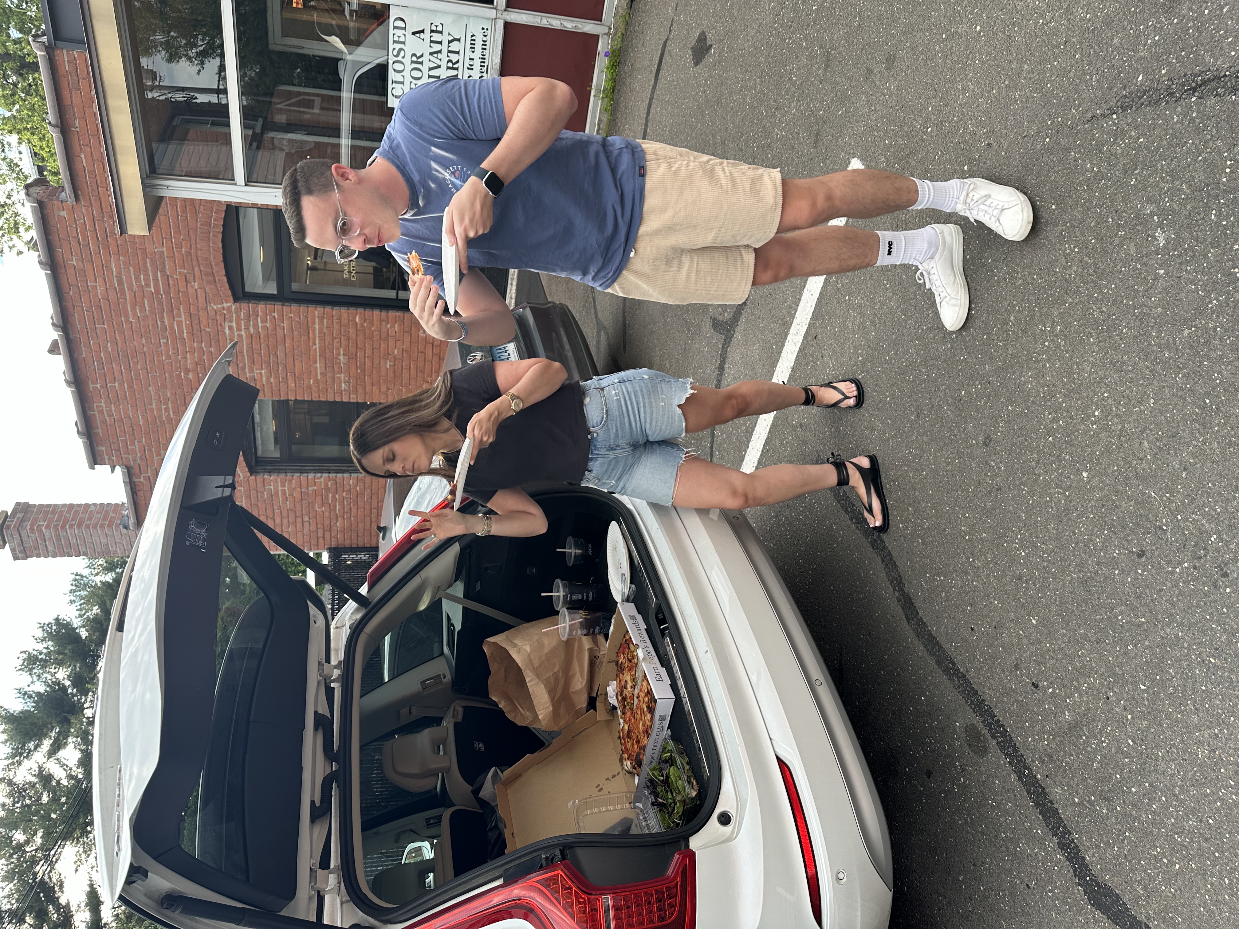 My wife perched in the back of our SUV and my brother-in-law standing beside it, eating Frank Pepe's pizza off the open tailgate before a Bleachers concert in New Haven.